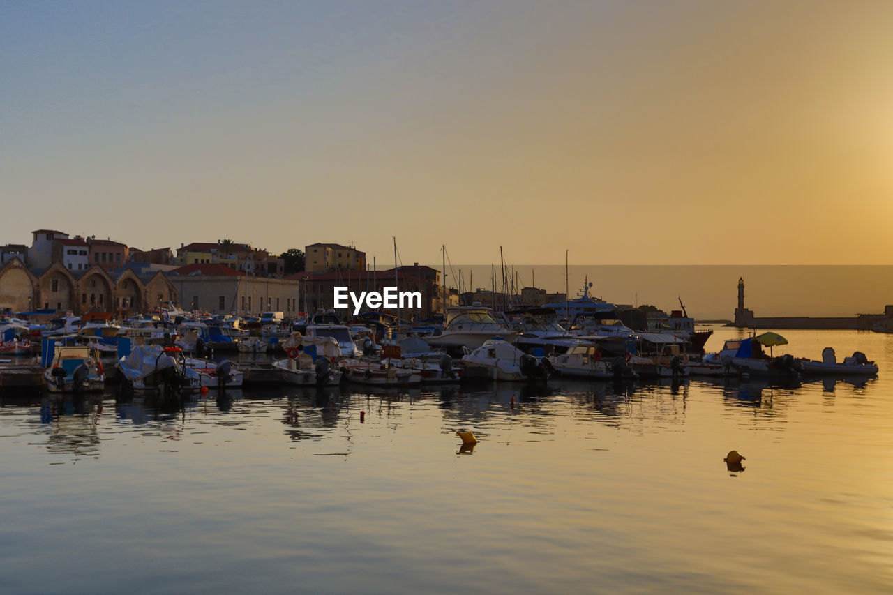 Boats moored in harbor at sunset