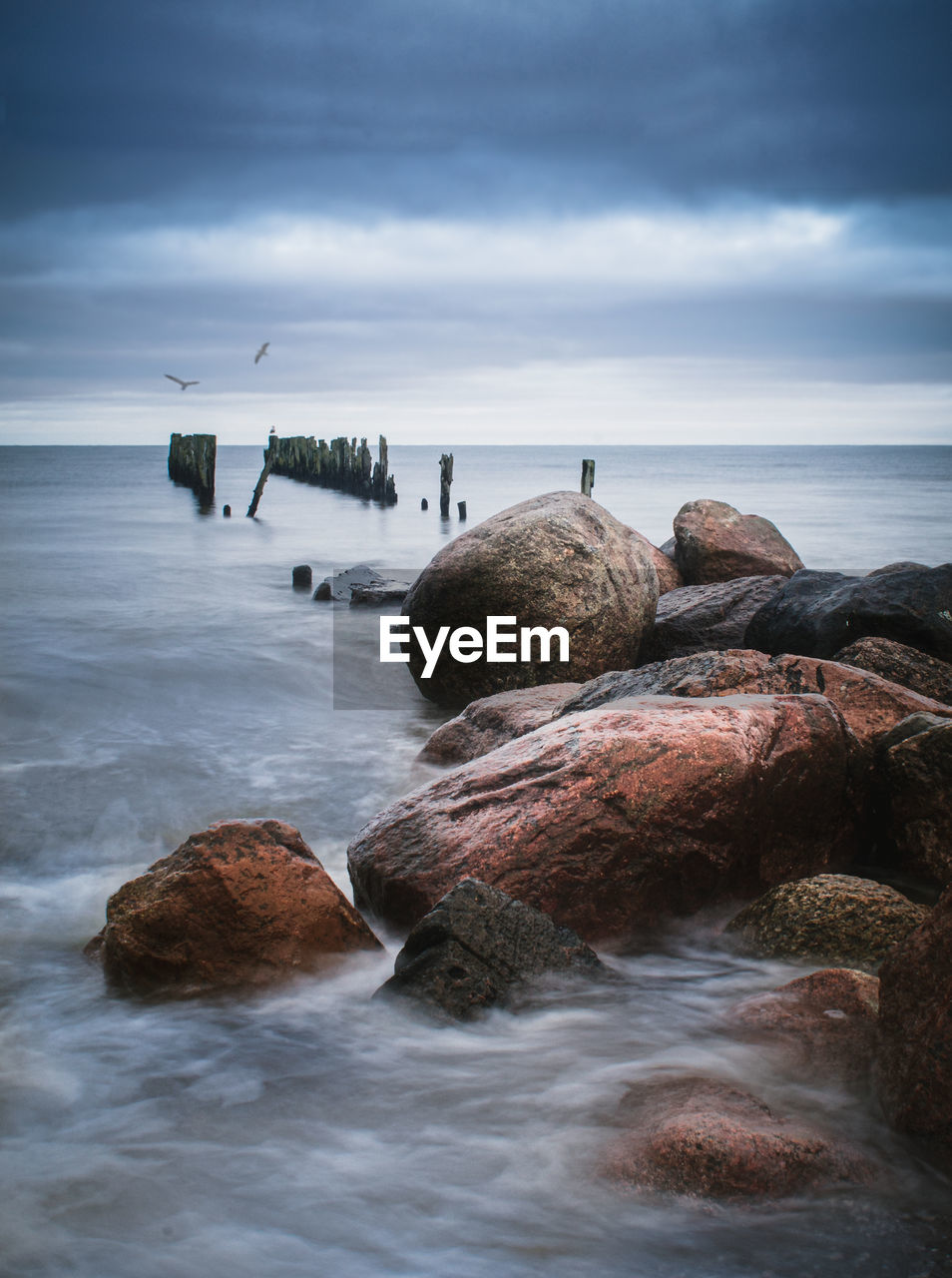 Rocks at beach against cloudy sky