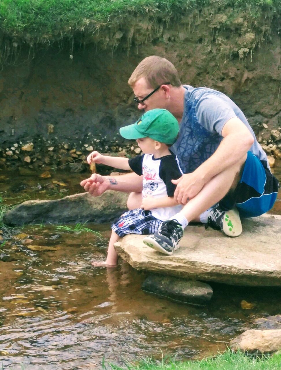 Father sitting with son by pond on rock