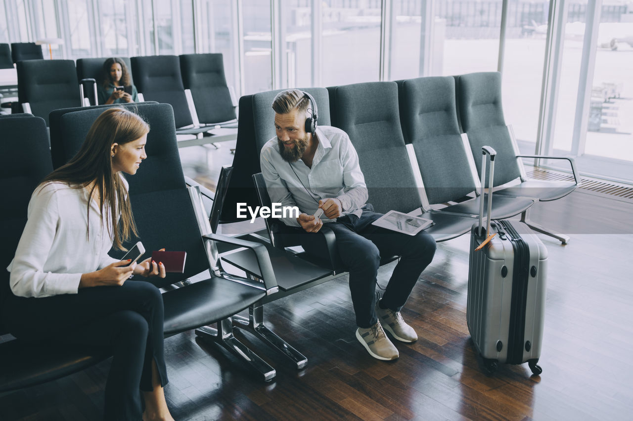 Smiling businessman talking to businesswoman while sitting at waiting room in airport