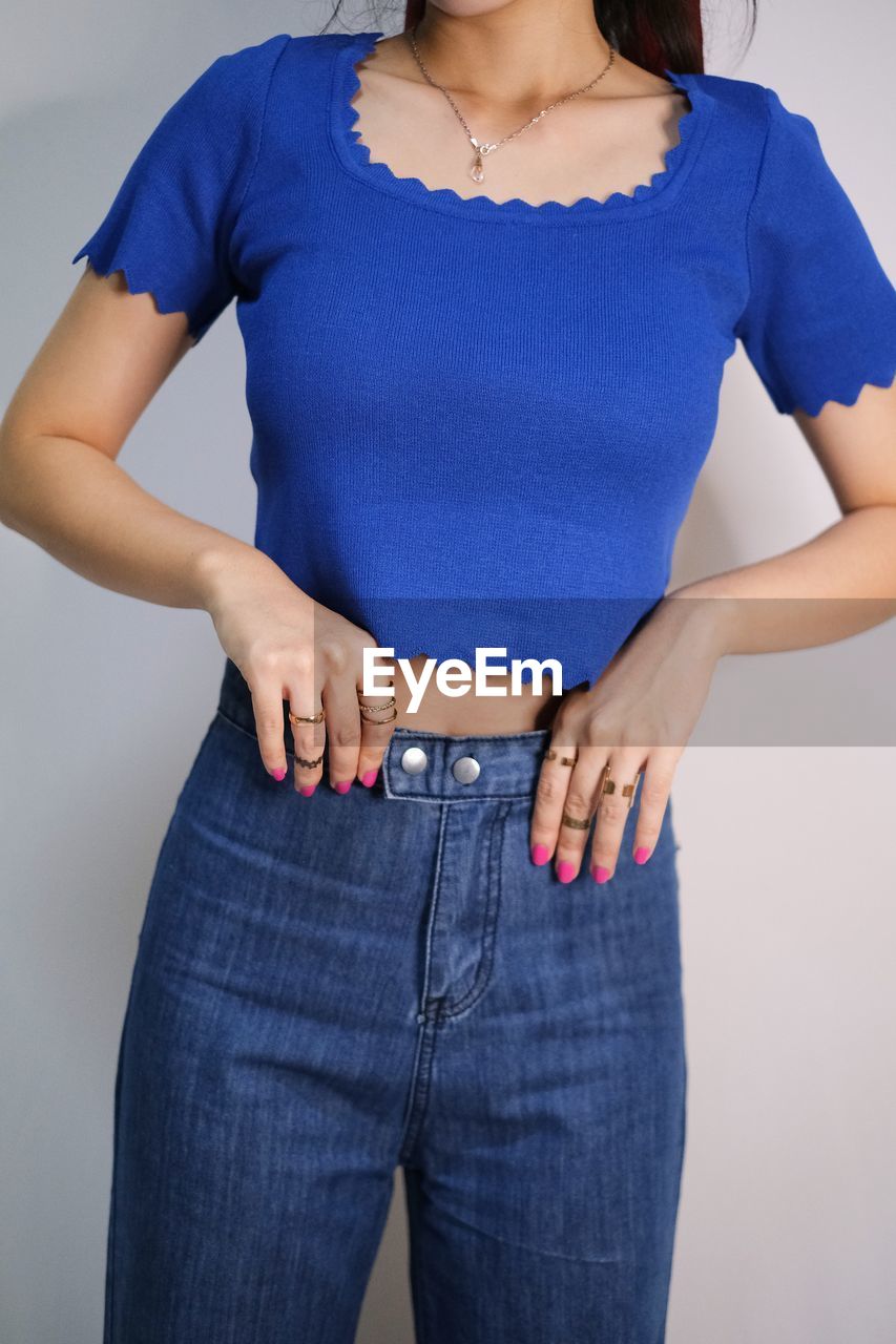 one person, adult, studio shot, women, casual clothing, clothing, indoors, blue, front view, standing, sleeve, jeans, hand, young adult, fashion, pocket, hand on hip, denim, female, portrait, t-shirt, midsection, trunk, gray, textile, colored background, emotion, gray background, child, three quarter length