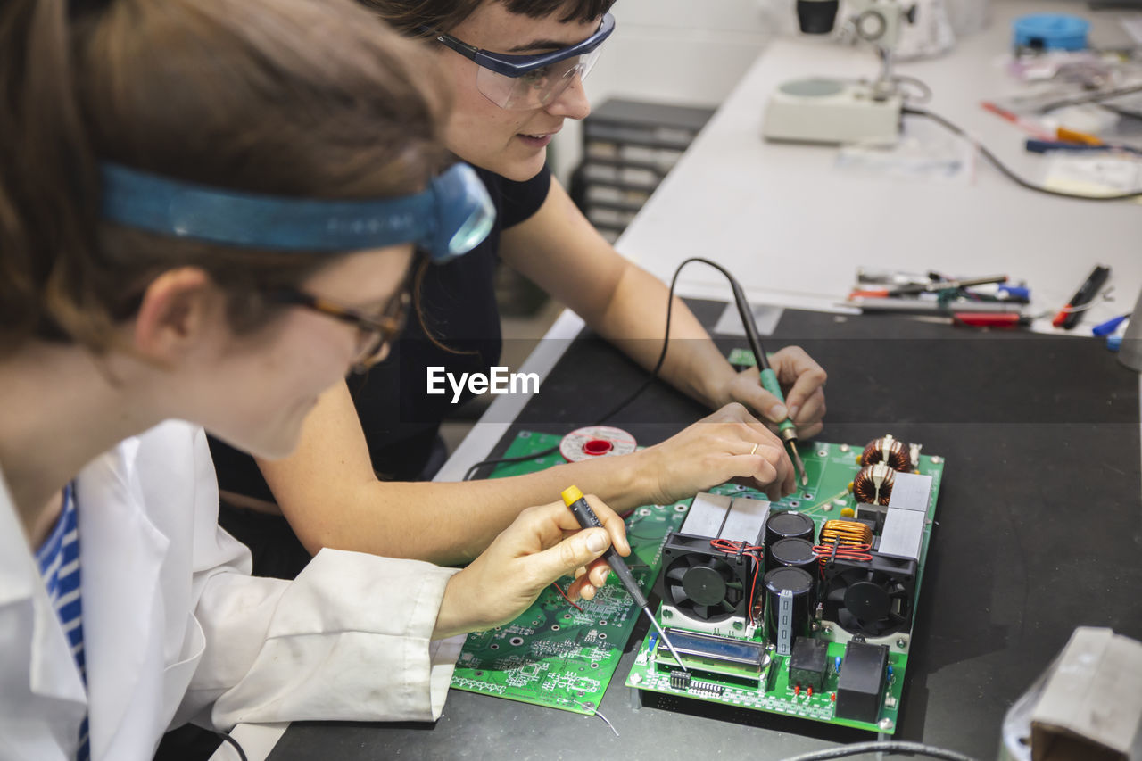 Female technicians soldering motherboard on table in workshop