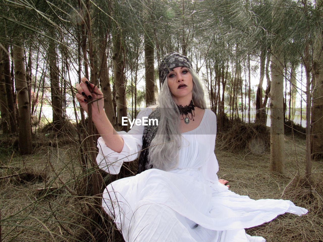 Portrait of woman in wedding dress sitting on field at forest