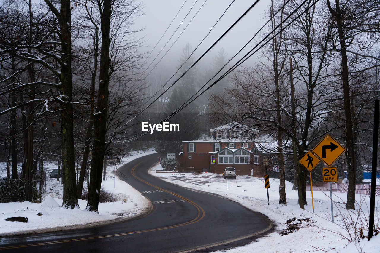 Road by snow covered trees against sky during winter