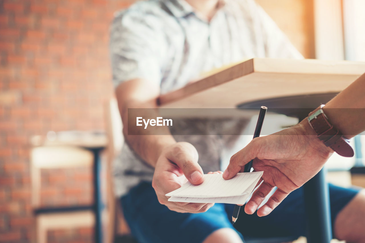 Midsection of man giving paper to person under table