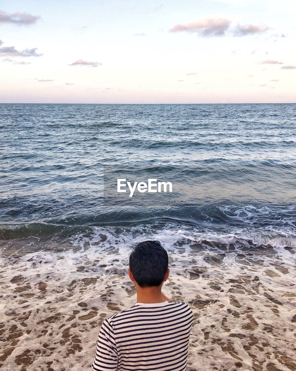 Rear view of man at beach against sky during sunset