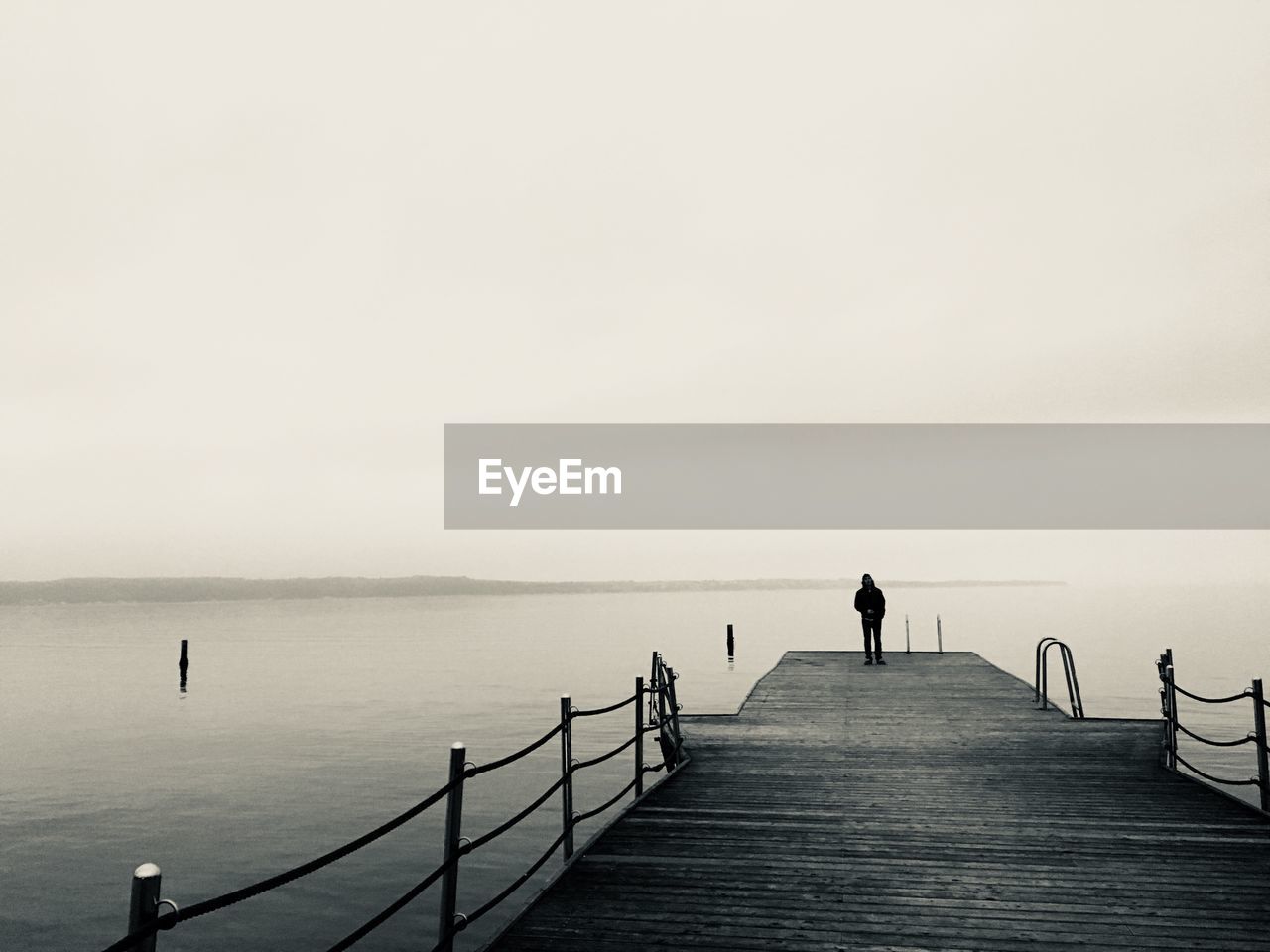 MAN STANDING BY RAILING AGAINST SEA