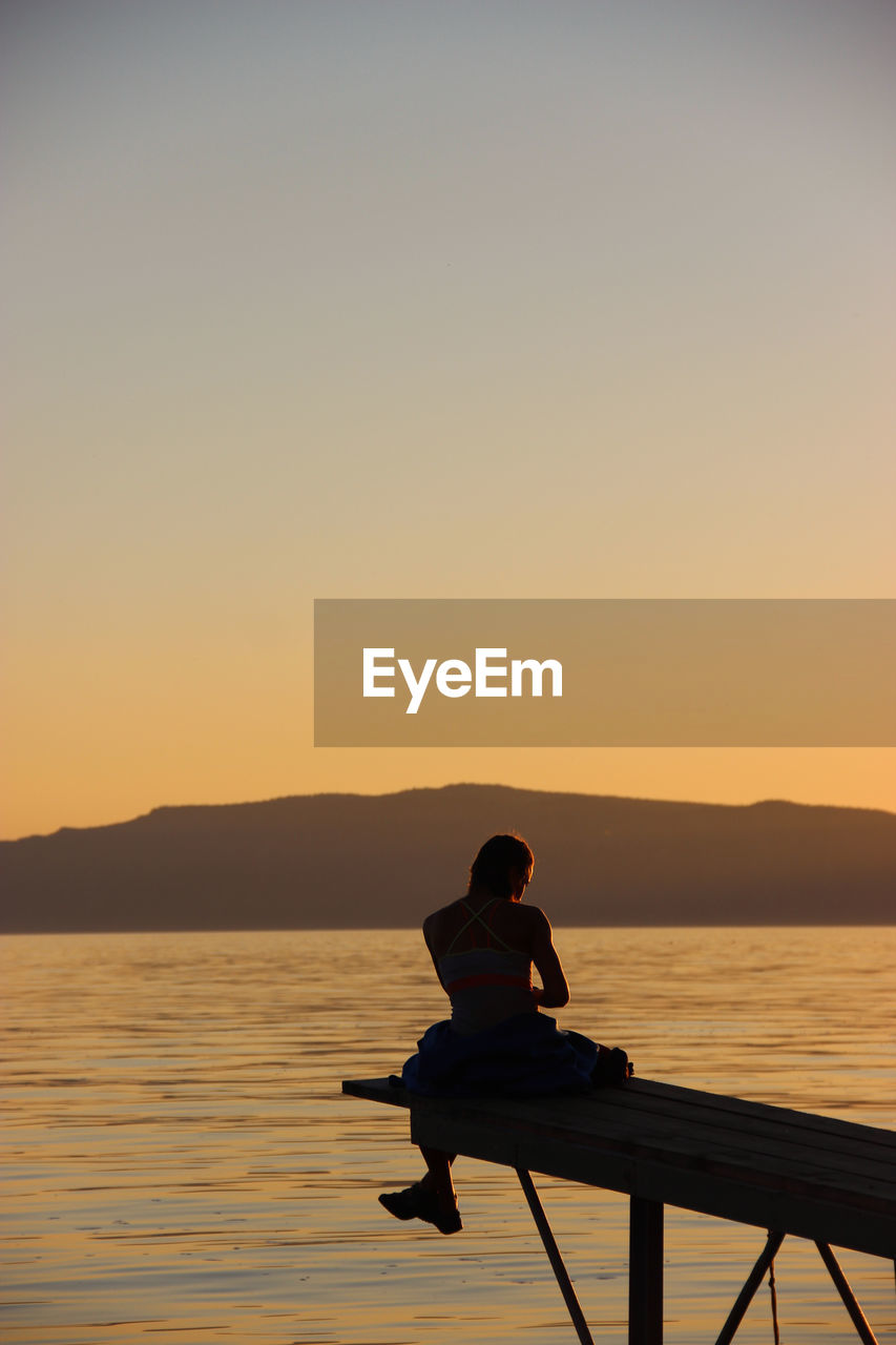 Silhouette man sitting on pier over sea against clear sky