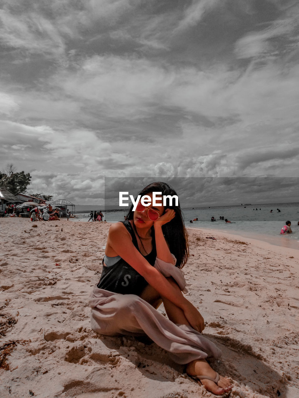Woman wearing sunglasses while sitting on beach against sky