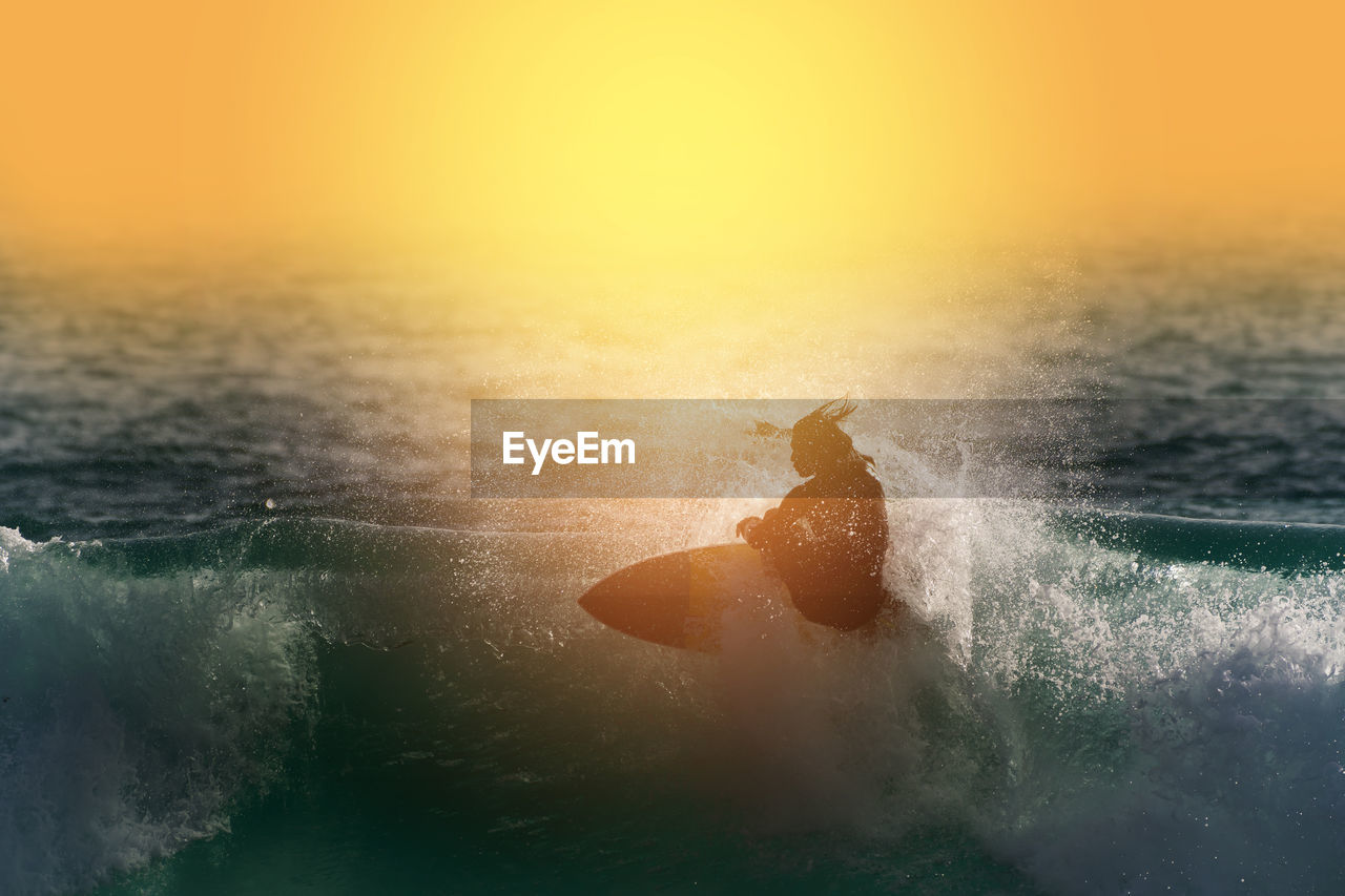 Man surfing in sea against sky during sunset