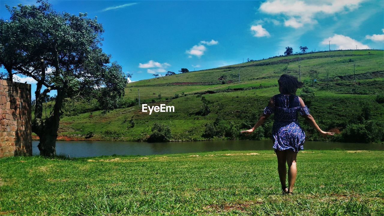 Rear view of woman walking on field against sky