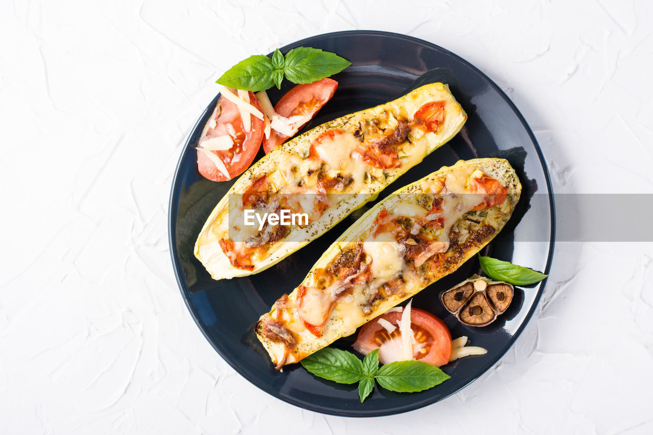 Ready-to-eat baked zucchini halves filled with cheese and tomato and basil leaves on a black plate 