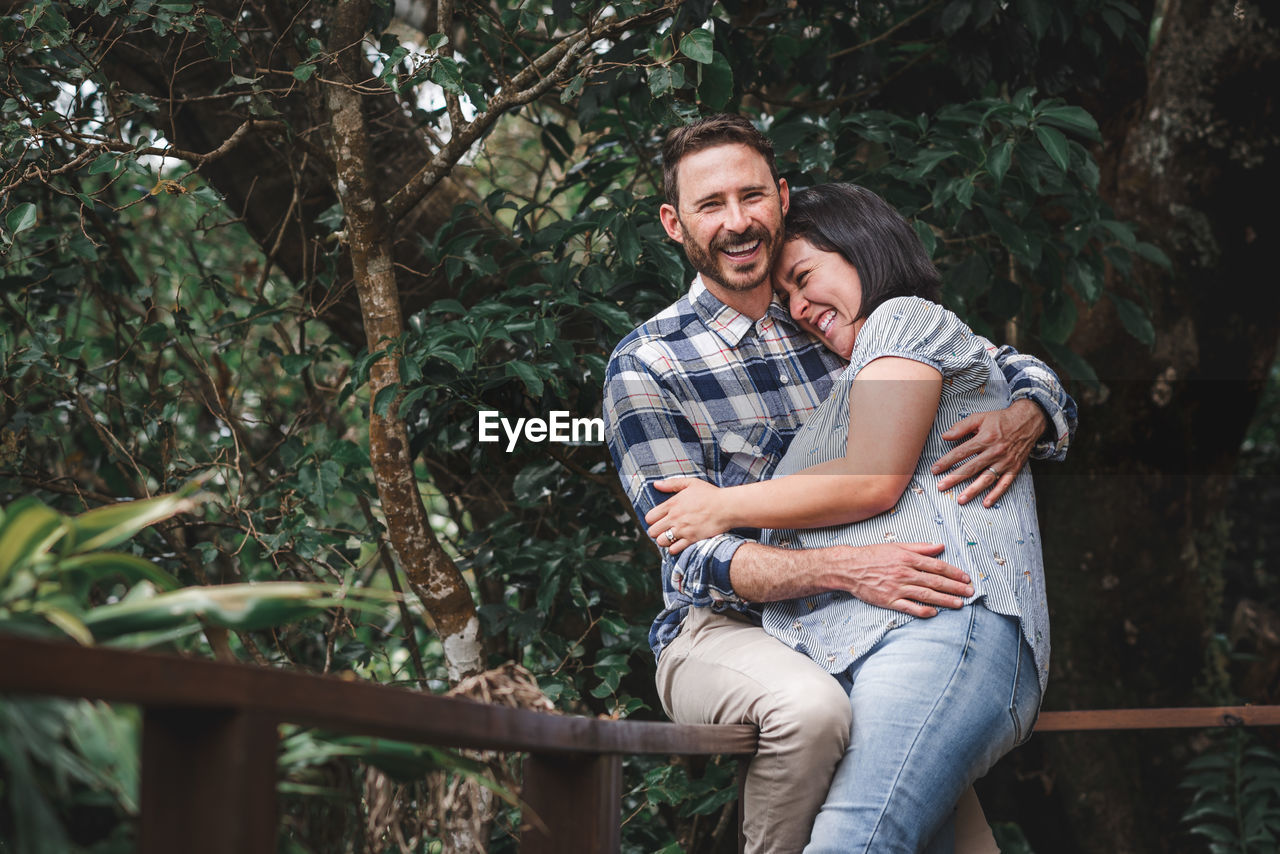 Cheerful couple in love embracing on wooden terrace of house in woods and laughing