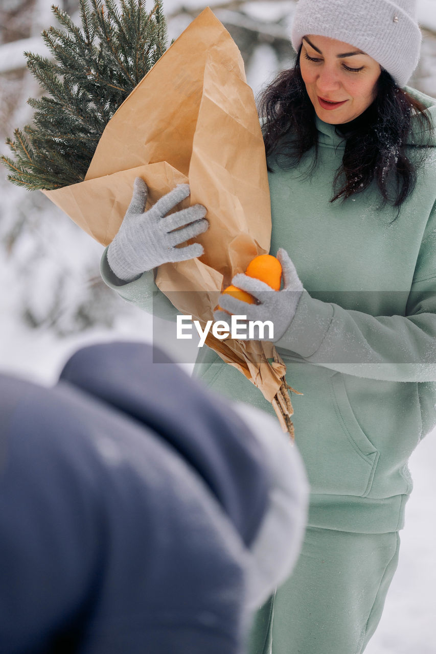 Happy couple playing winter game in forest outdoors. boyfriend gives girlfriend bouquet of spruce 