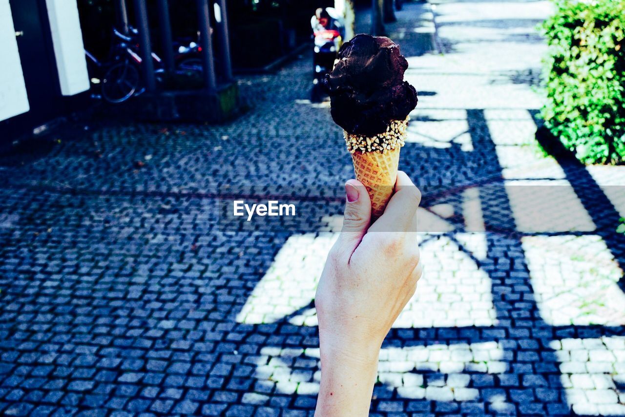 Cropped hand of woman holding ice cream over footpath