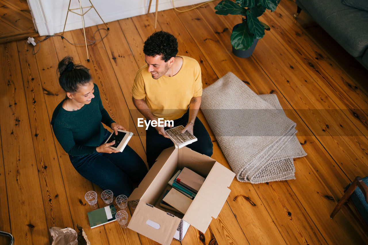 Smiling couple removing novels from box in living room at new home