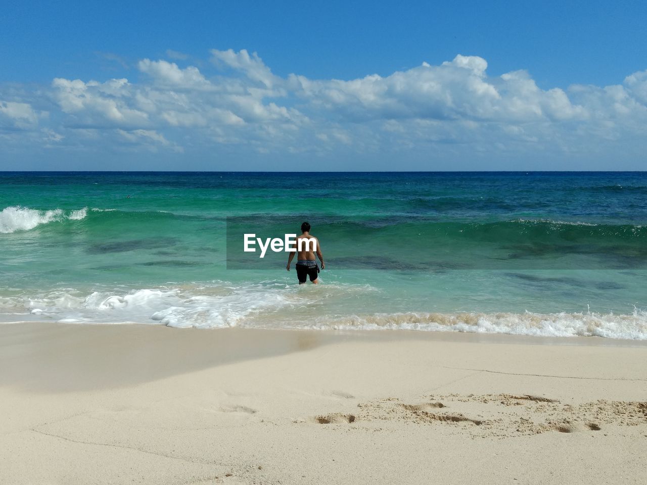 Rear view of man standing at beach against sky