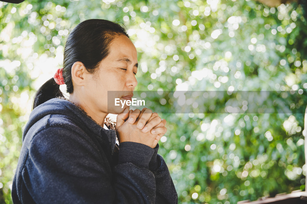 Woman praying in nature, the girl thanks god with her hands folded at her chin,.