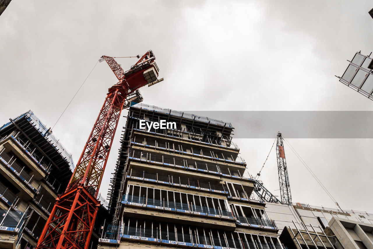 Low angle view of crane by building against sky