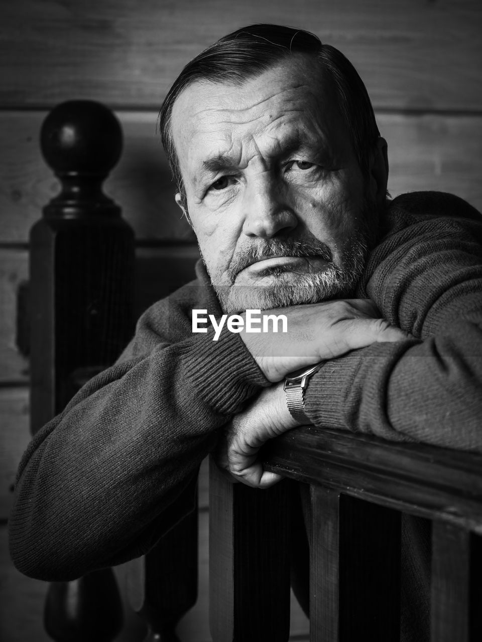 Portrait of senior man wearing sweater leaning on wooden railing while sitting at home