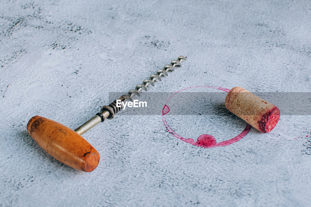 Vintage corkscrew, cork and red wine stain or ring over gray background.