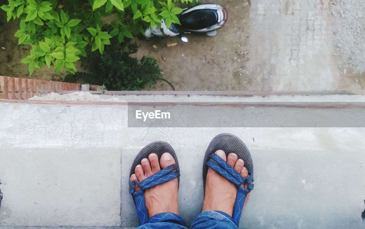 Low section of man wearing sandals standing on retaining wall