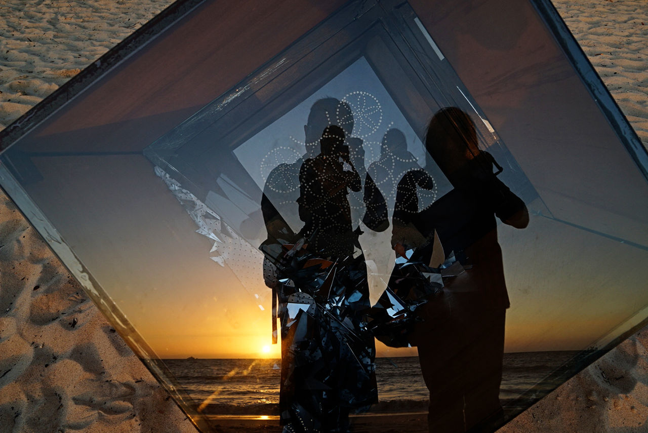 People reflecting in glass at beach