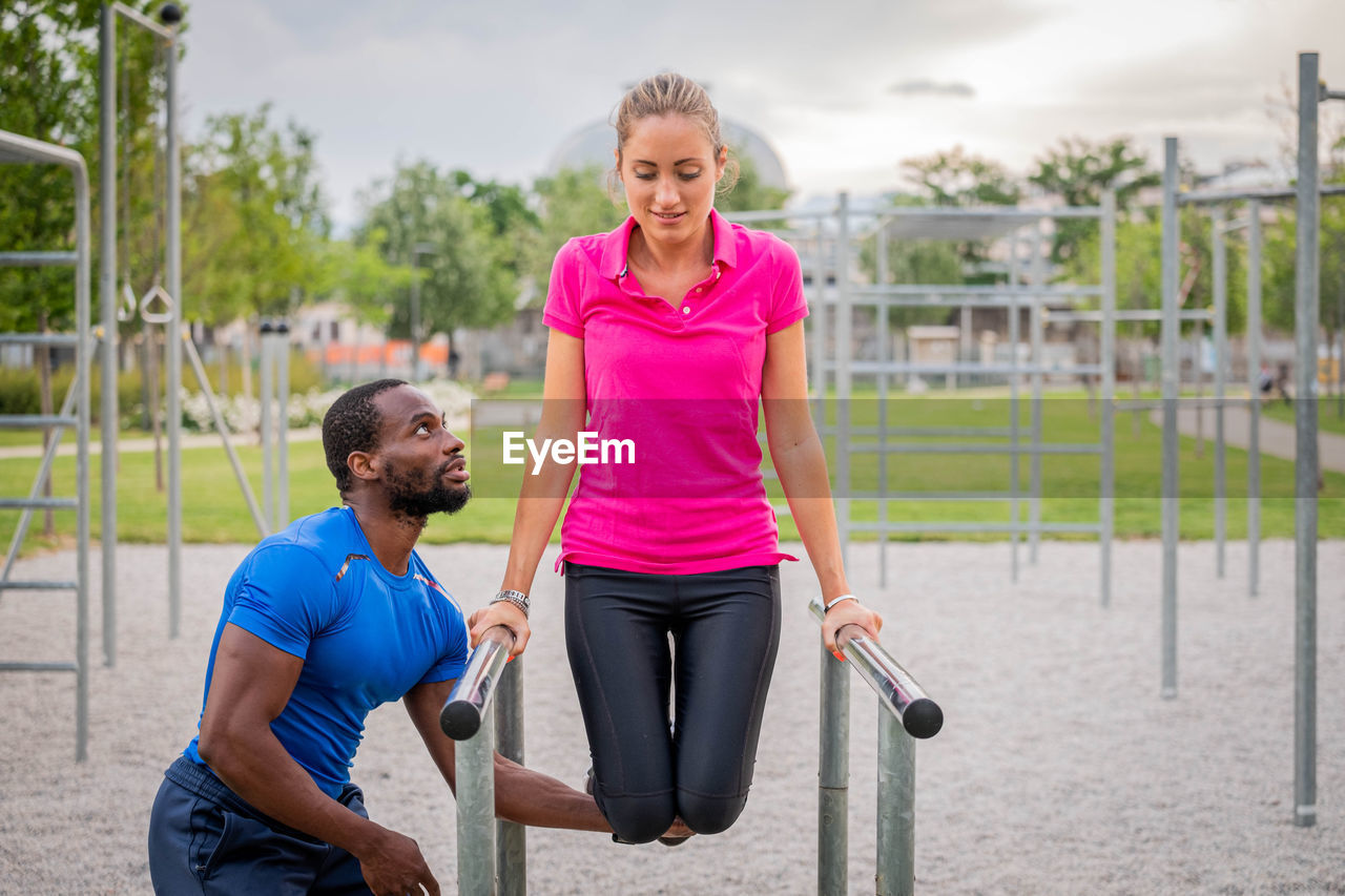 Afro american fitness instructor coaching helping woman doing push-ups on cross fit horizontal bar 