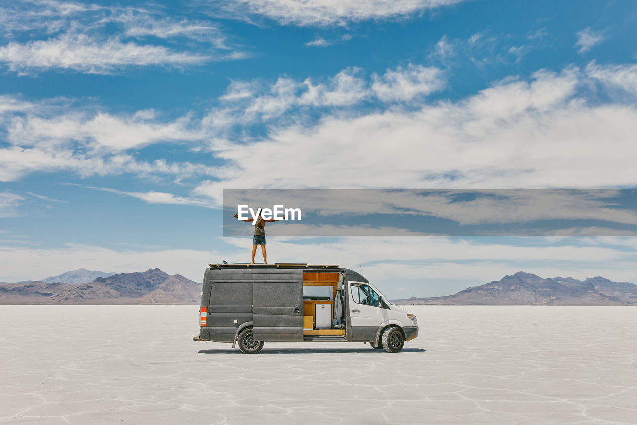 Young man standing on roof of camper van in bonneville salt flats.