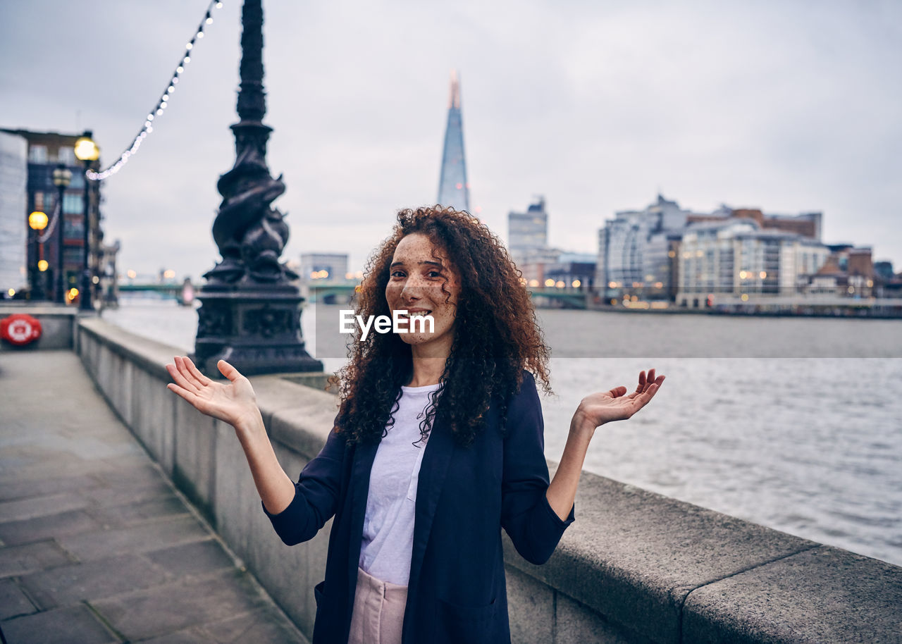 Portrait of woman gesturing while standing against thames river in city