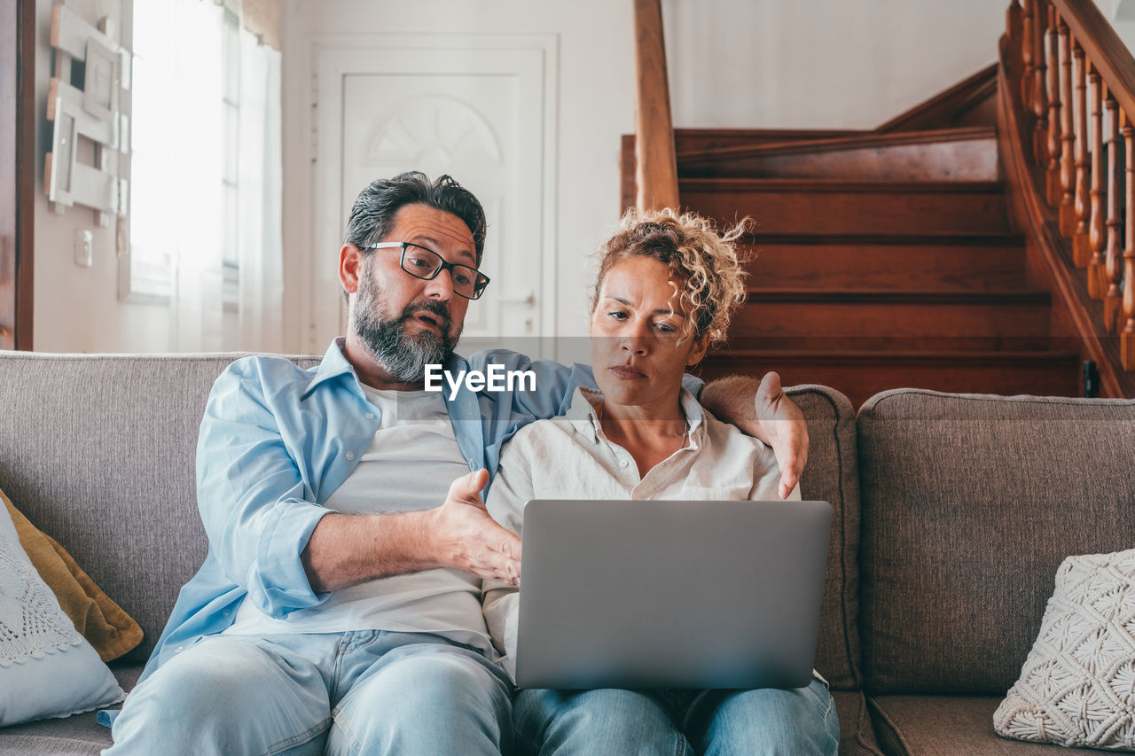 Serious couple looking at laptop while sitting on sofa