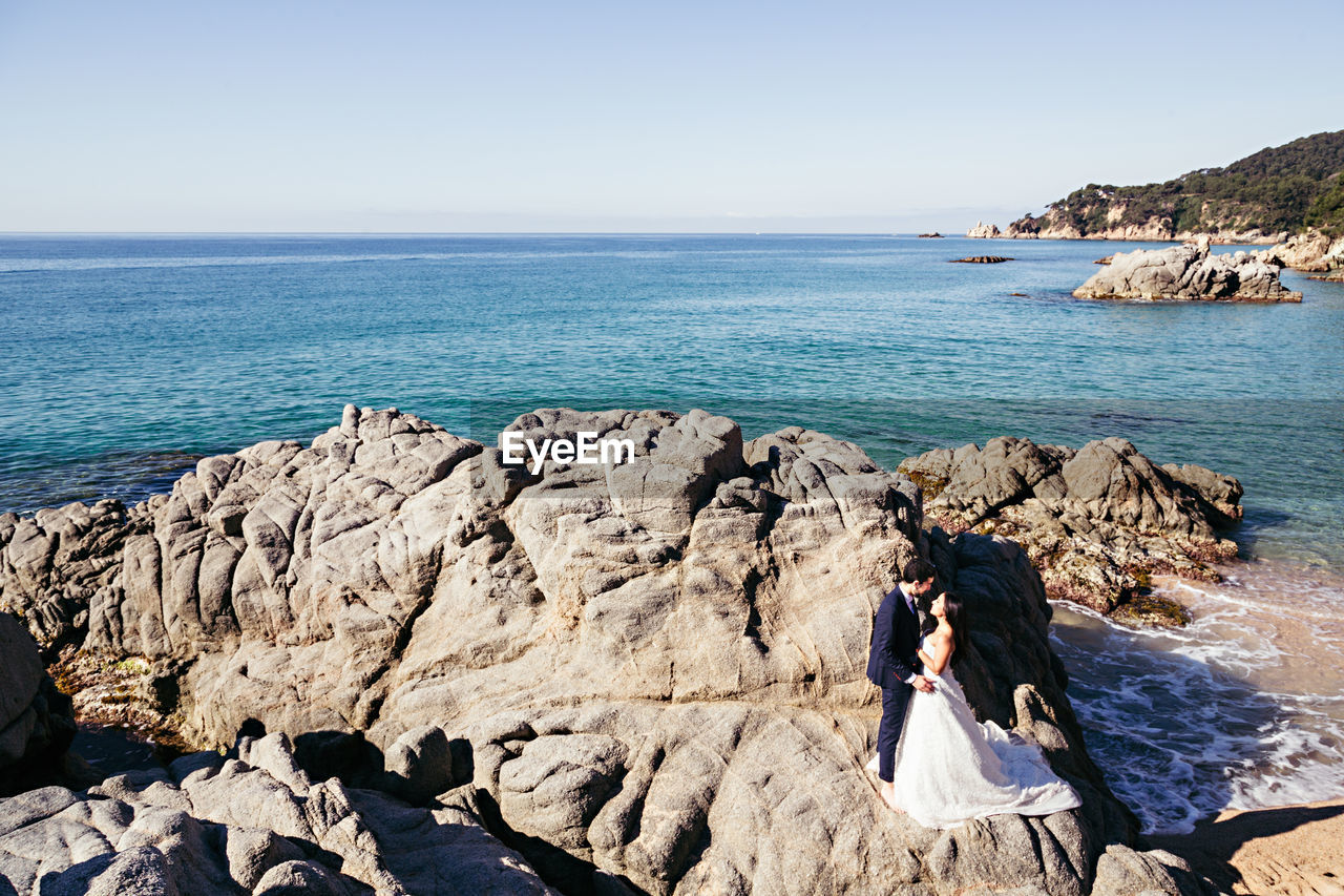 High angle view of newlywed couple romancing at beach against clear sky during sunny day