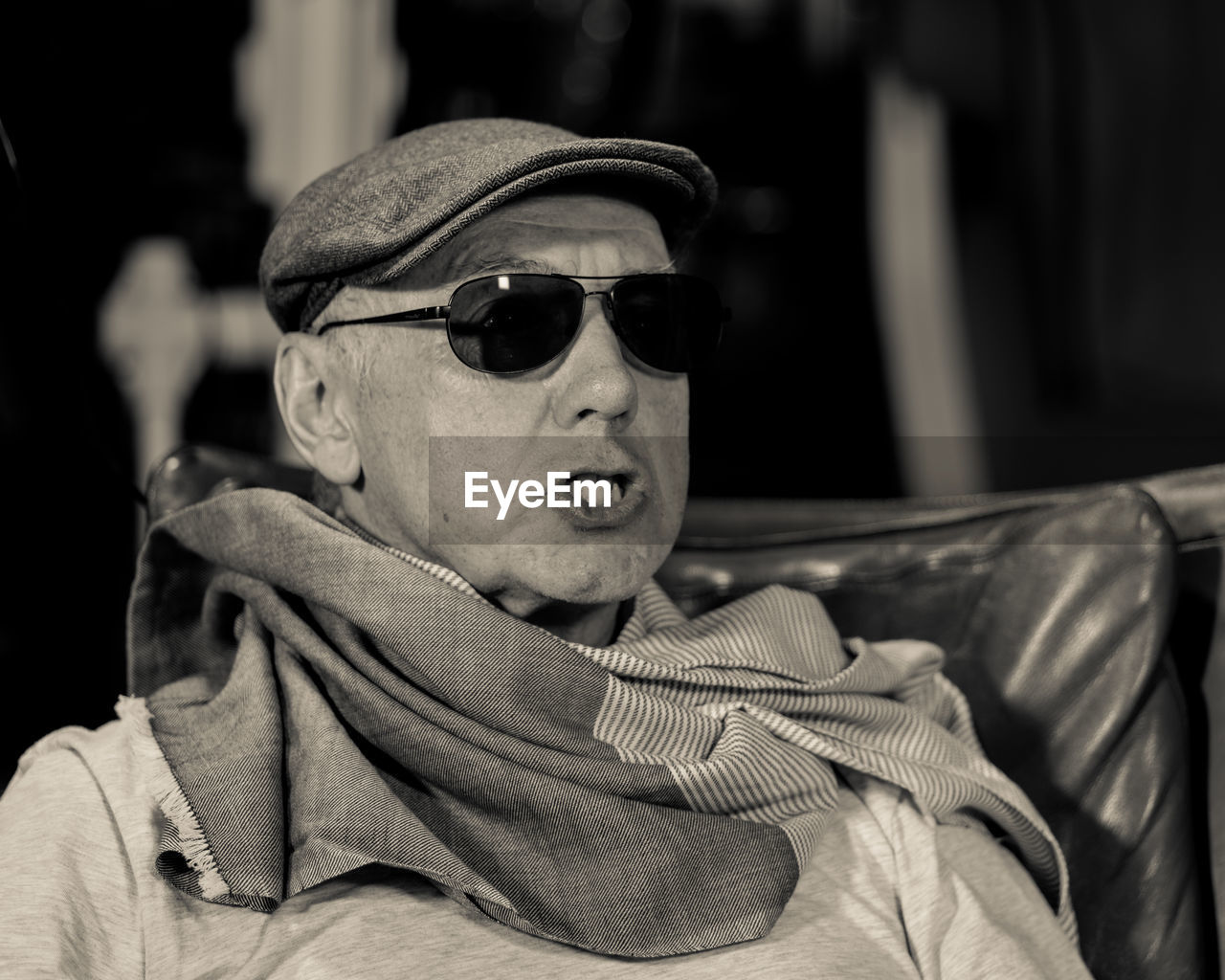 Close-up of senior man in sunglasses and cap making face while sitting on chair