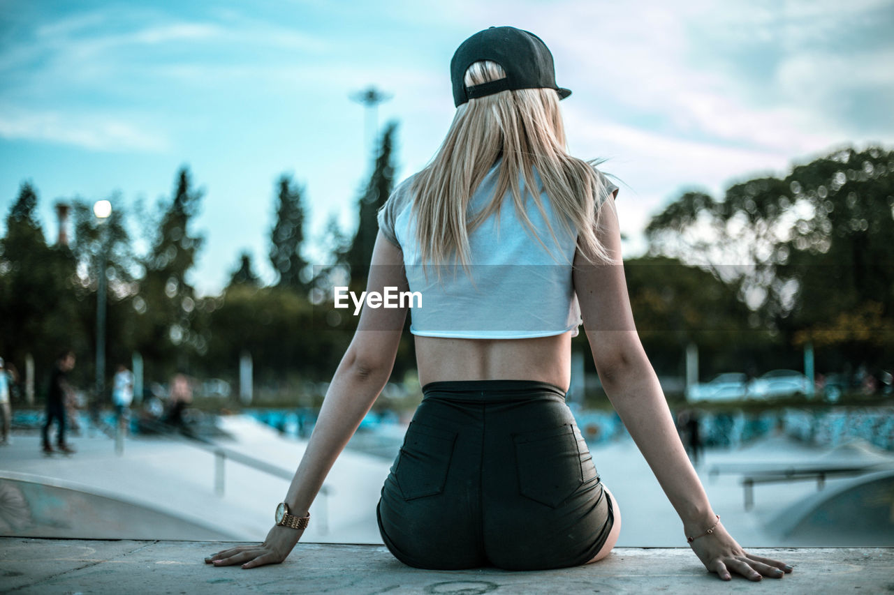 Rear view of young woman sitting at poolside