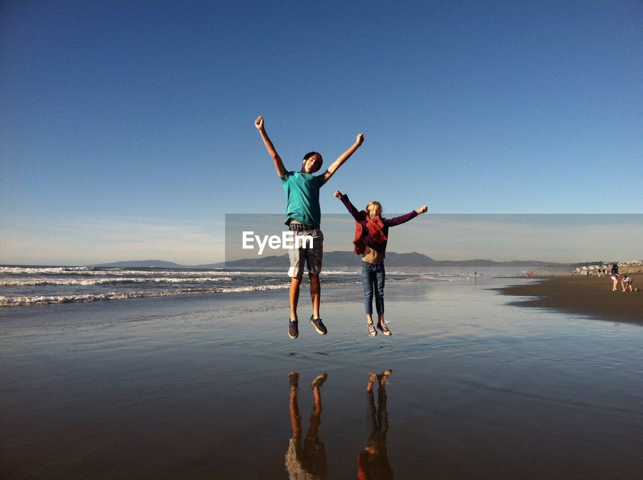 Full length of brother and sister jumping at beach