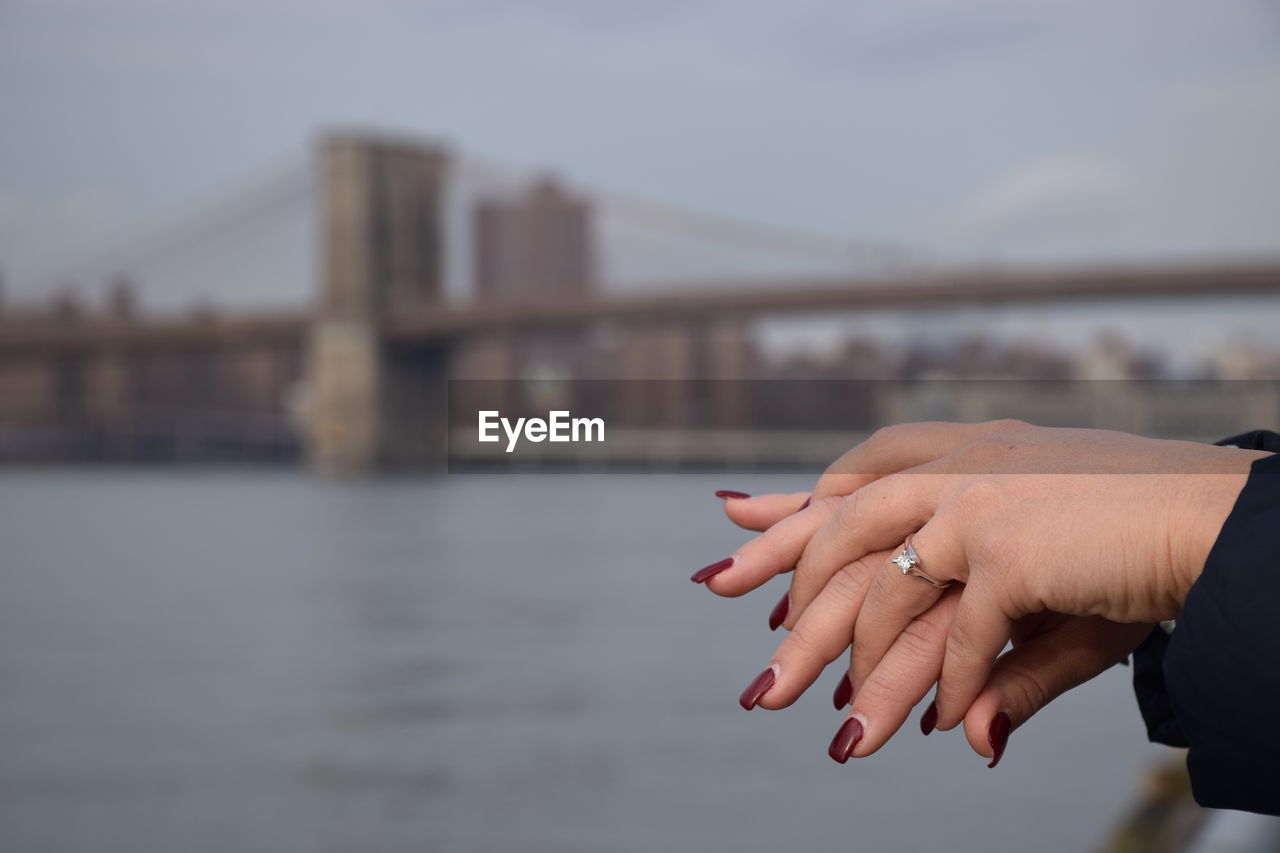 Cropped image of hands with a ring against bridge over river