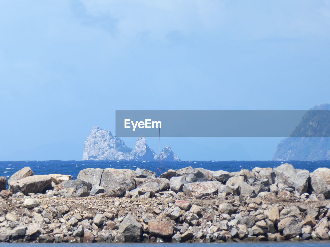 Rocks by sea against clear blue sky