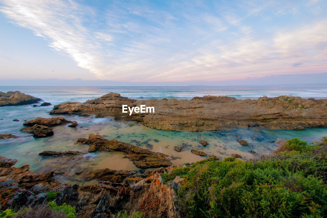 Rocks against sea under cloudy sky