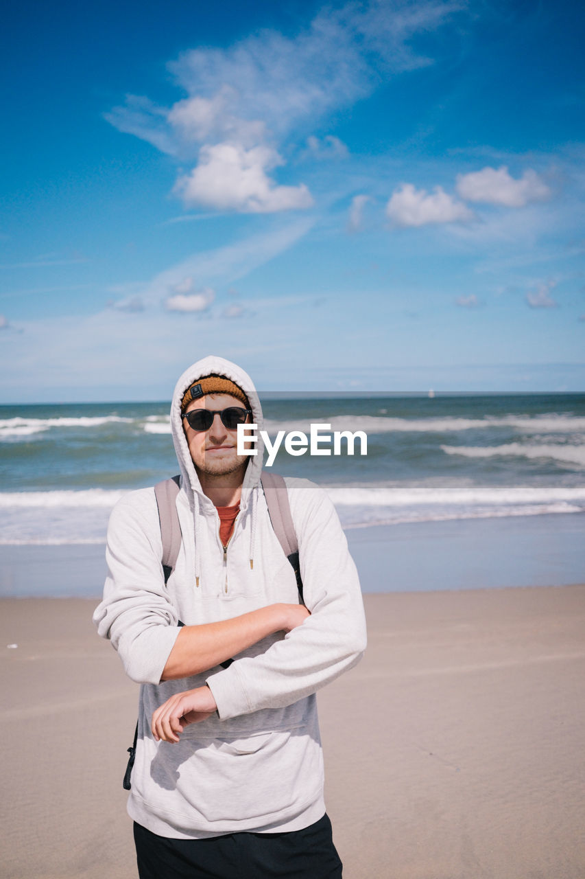 PORTRAIT OF MAN WEARING SUNGLASSES STANDING AT BEACH