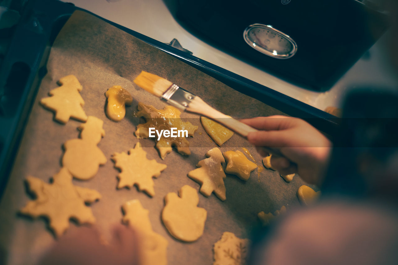 Child coating christmas cookies on a baking sheet with egg yolk.
