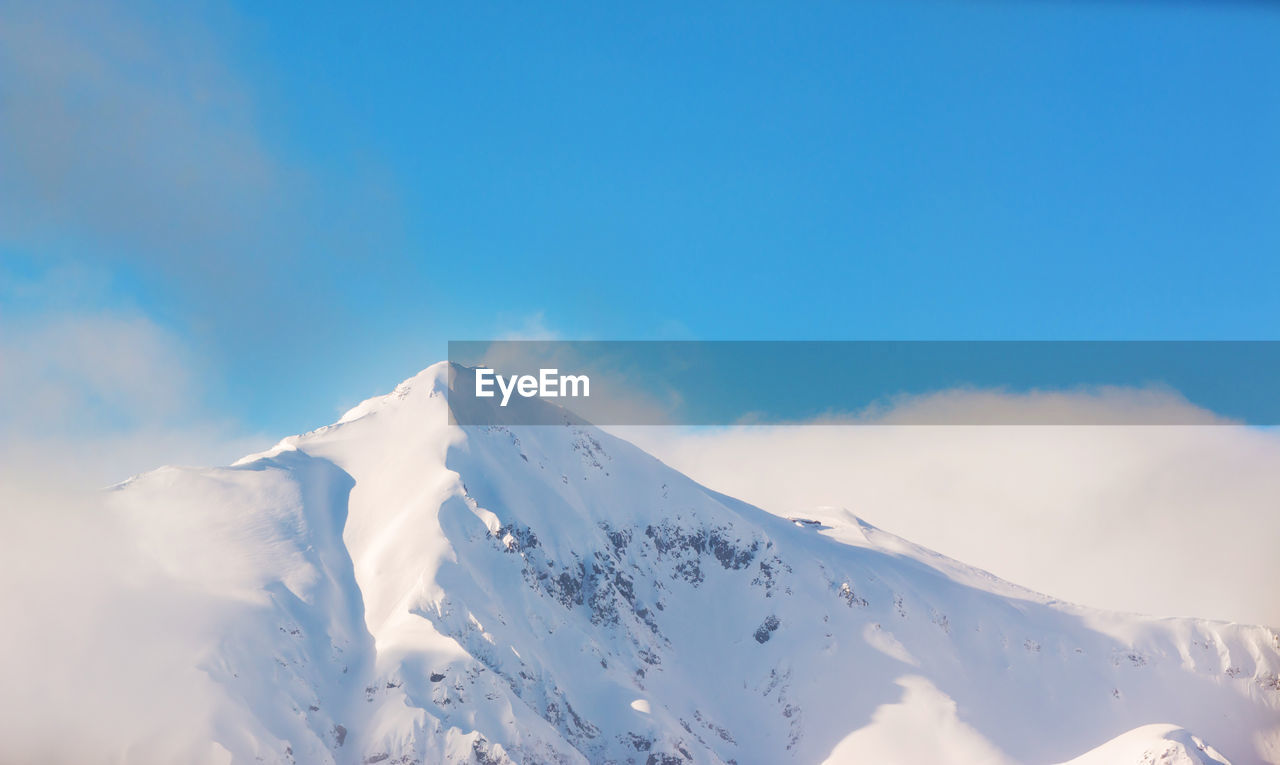 Low angle view of snowcapped mountains against blue sky