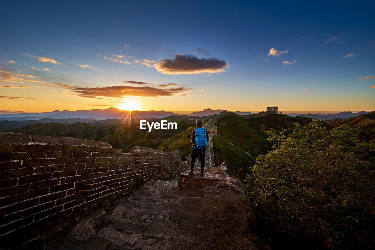 Rear view of person standing by great wall of china against sky during sunset