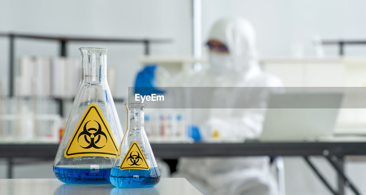 Erlenmeyer flask contains blue liquid chemicals on a white laboratory table.