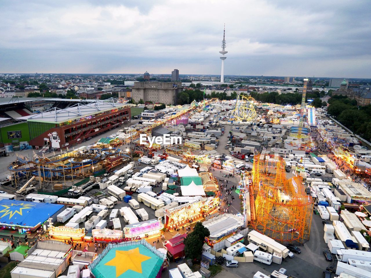 Funfair by heinrich-hertz-turm in city against cloudy sky