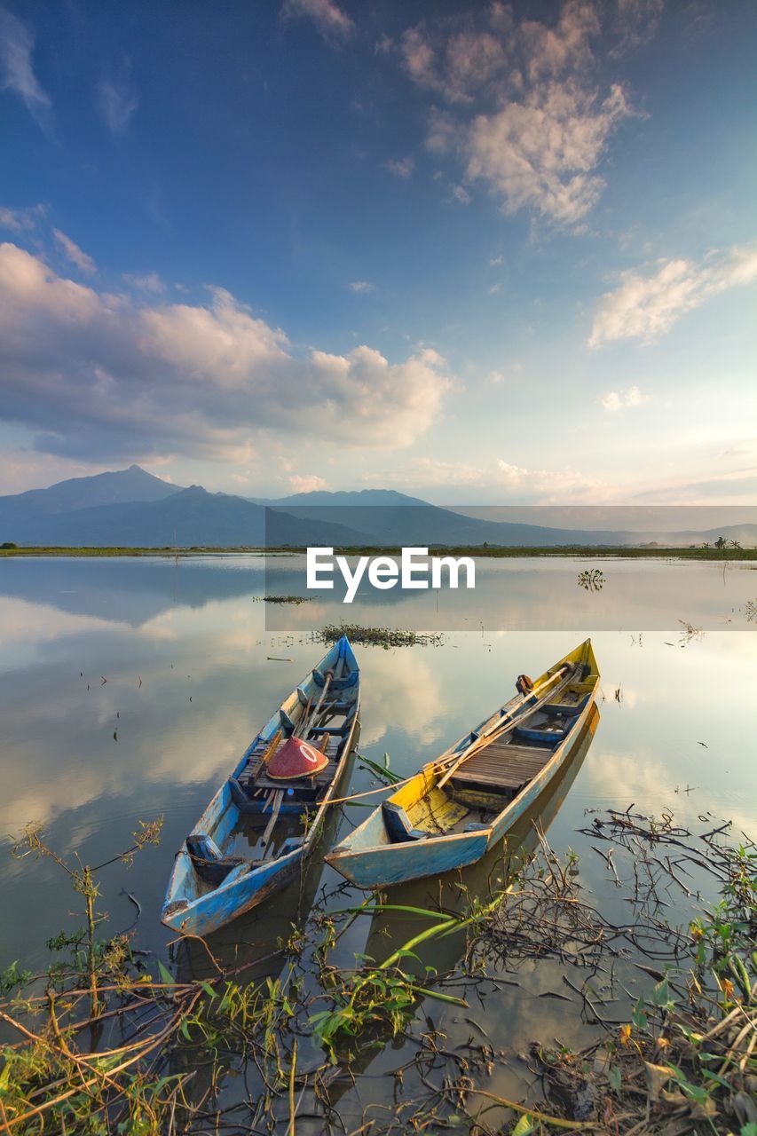 Fishing boats moored on lake against sky