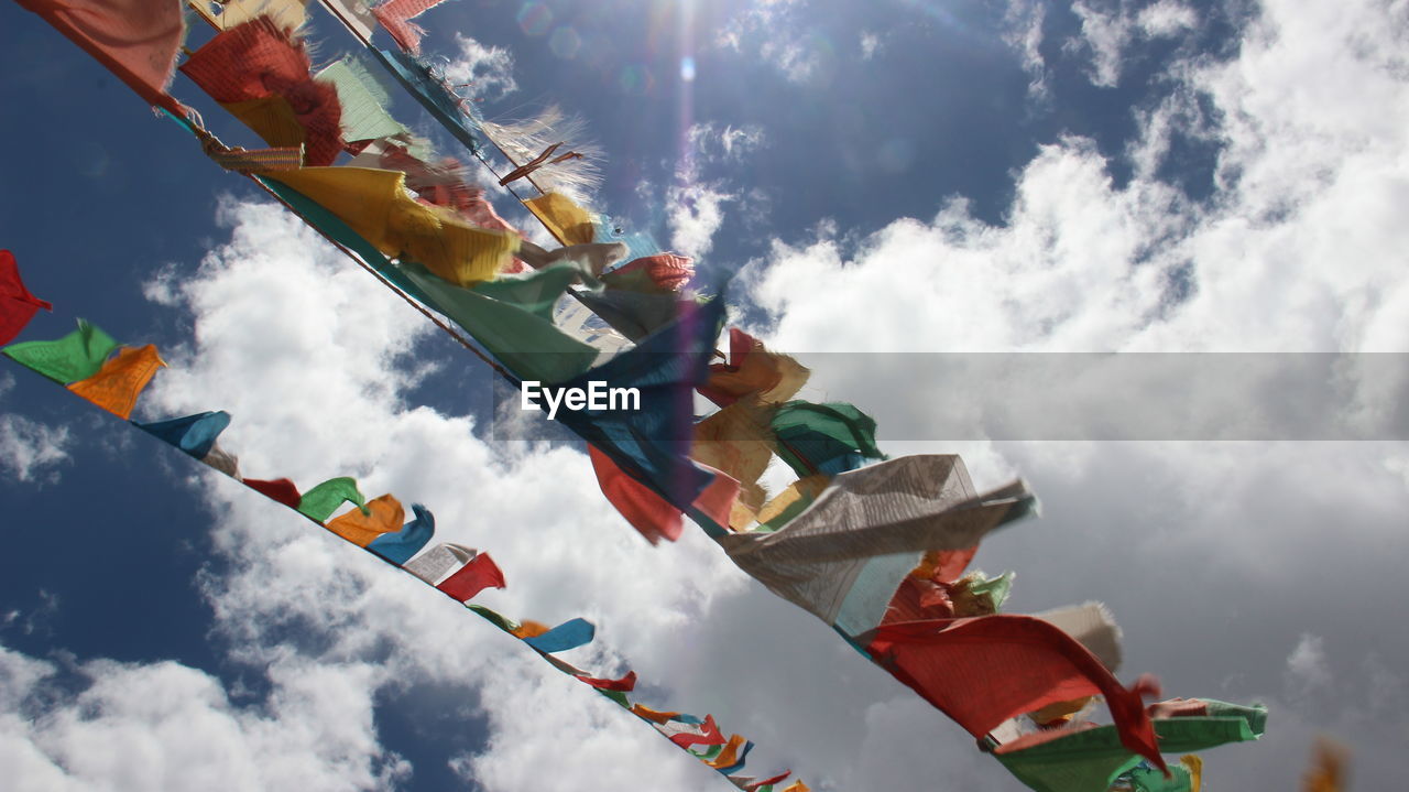 Low angle view of multi colored prayer flags waving against sky