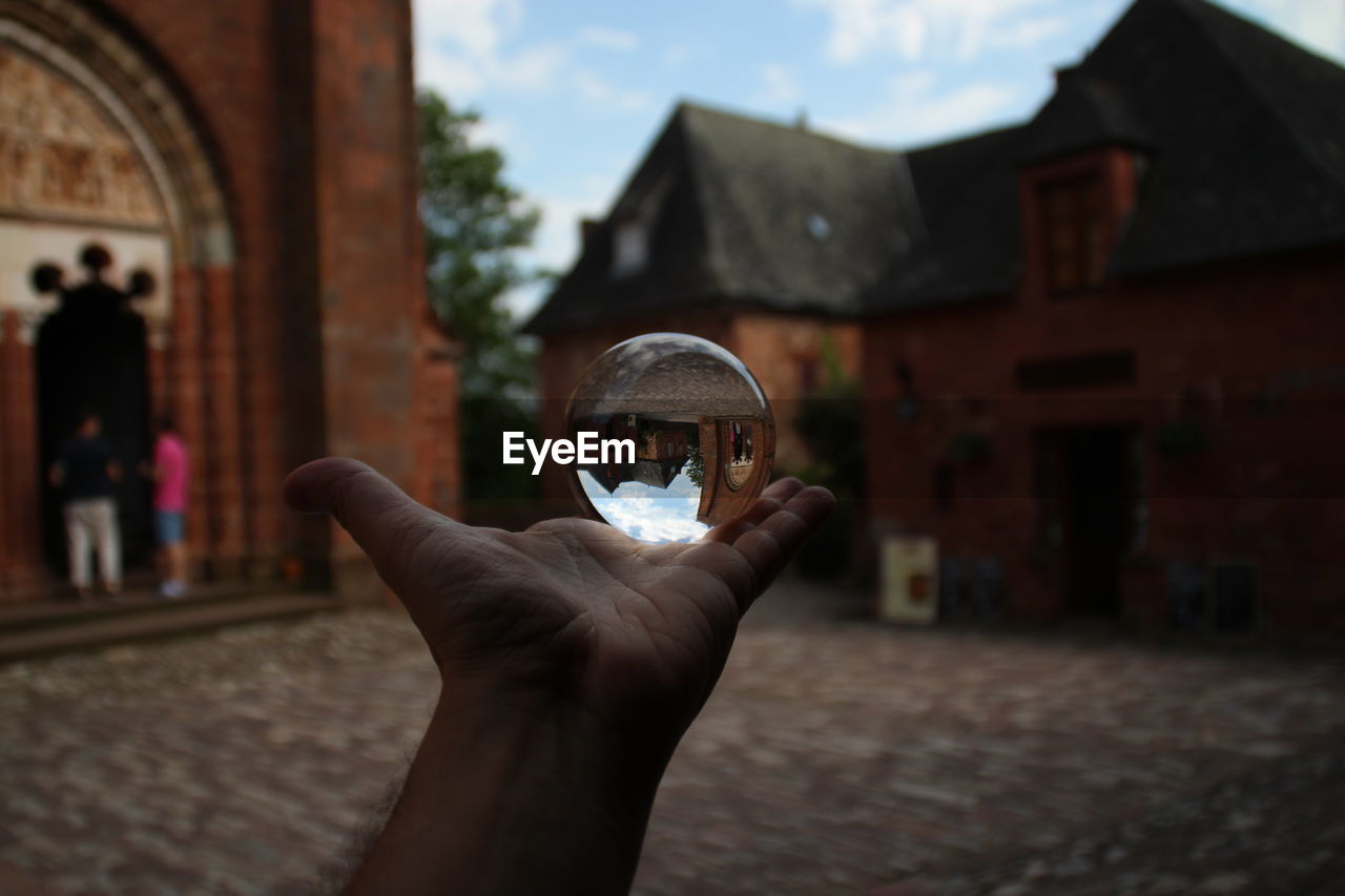 Cropped image of hand holding crystal ball with reflection of buildings