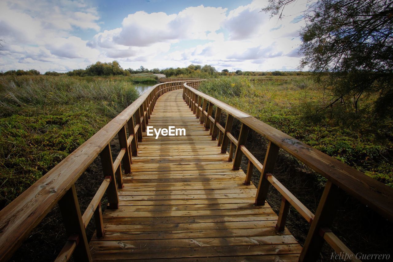 Surface level of wooden footbridge on landscape against sky