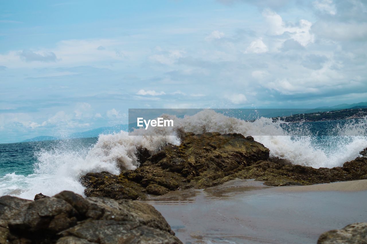 Waves splashing on rocks at shore against sky