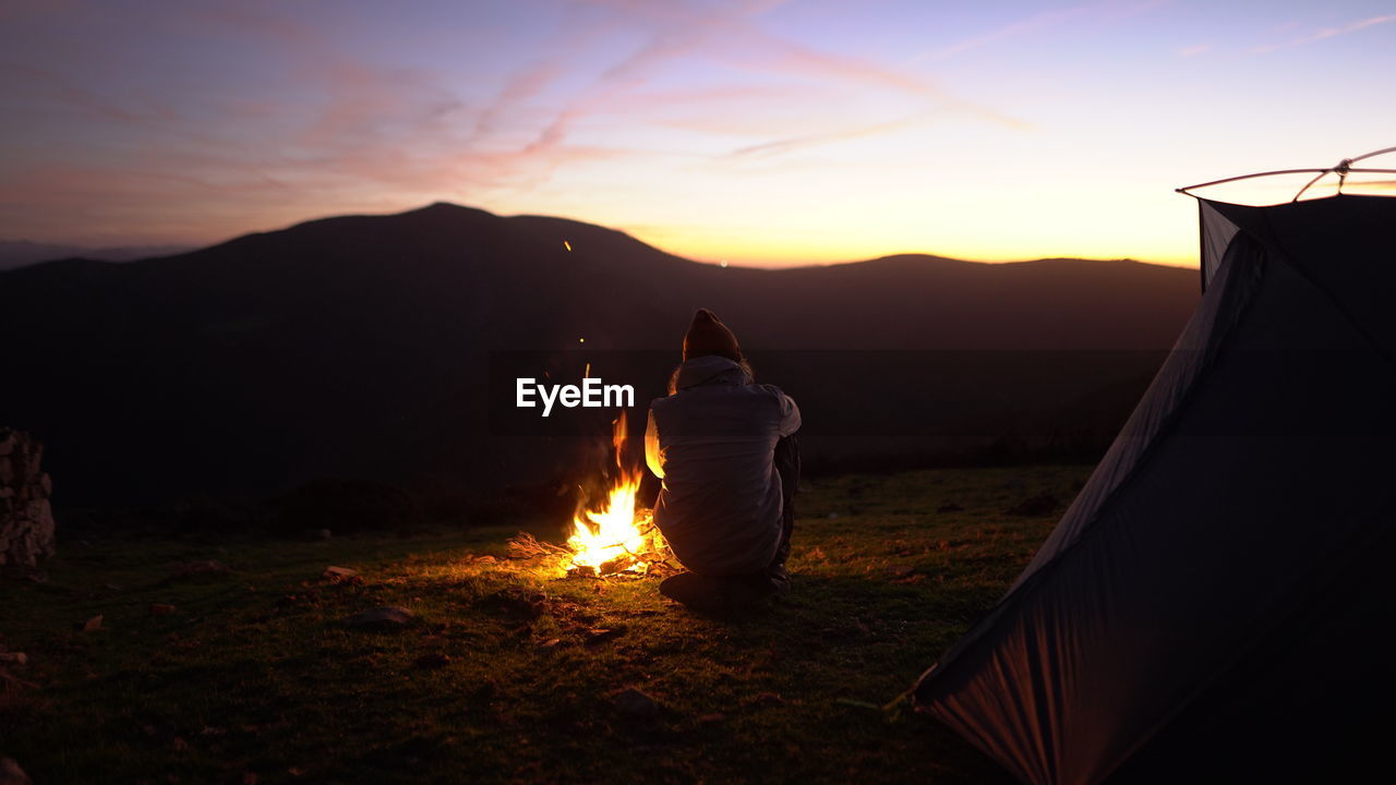 Man enjoys a campfire with sunset view next to a tent